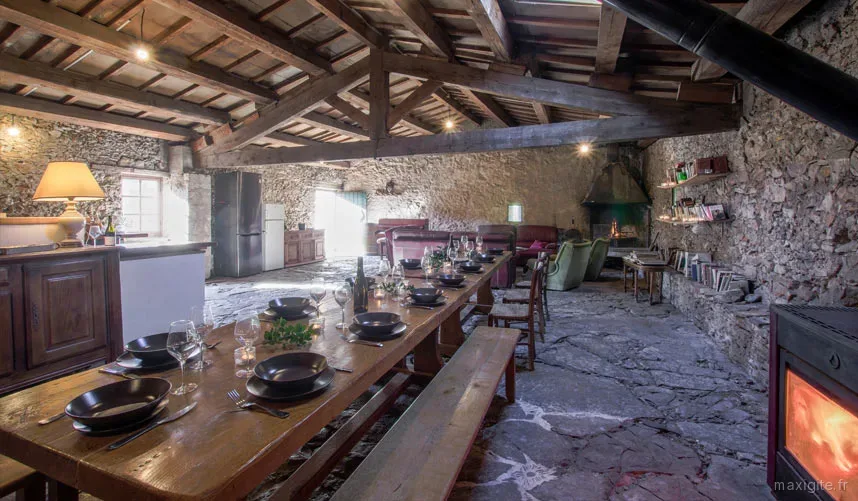 Grande table conviviale sous charpente en bois, avec cheminée pour les repas en tribu