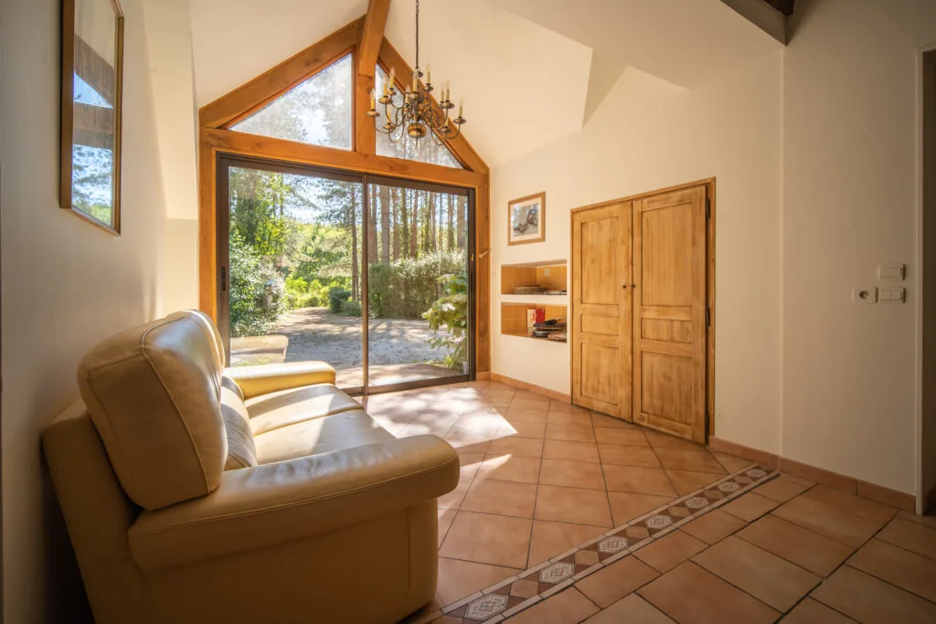 Salon lumineux avec grande baie vitrée triangulaire en bois donnant sur le jardin verdoyant