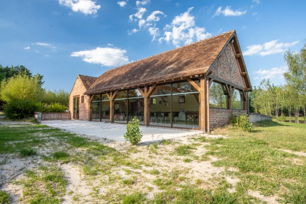 Salle de réception extérieure en bois et verre avec terrasse dallée, prairie alentour