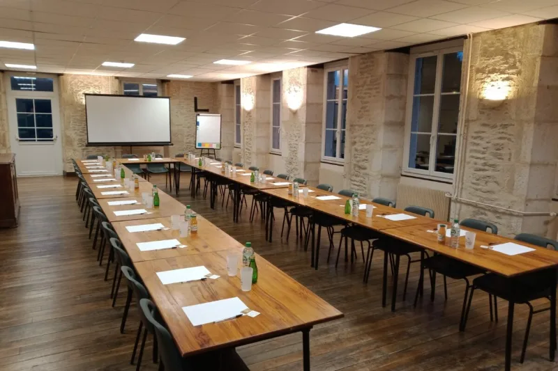 Salle de séminaire en configuration U avec écran de projection, tables et murs en pierre de la ferme