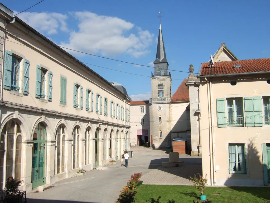 Cour intérieure du Centre d'Accueil de Benoîte-Vaux avec arcades, volets verts et clocher en arrière-plan