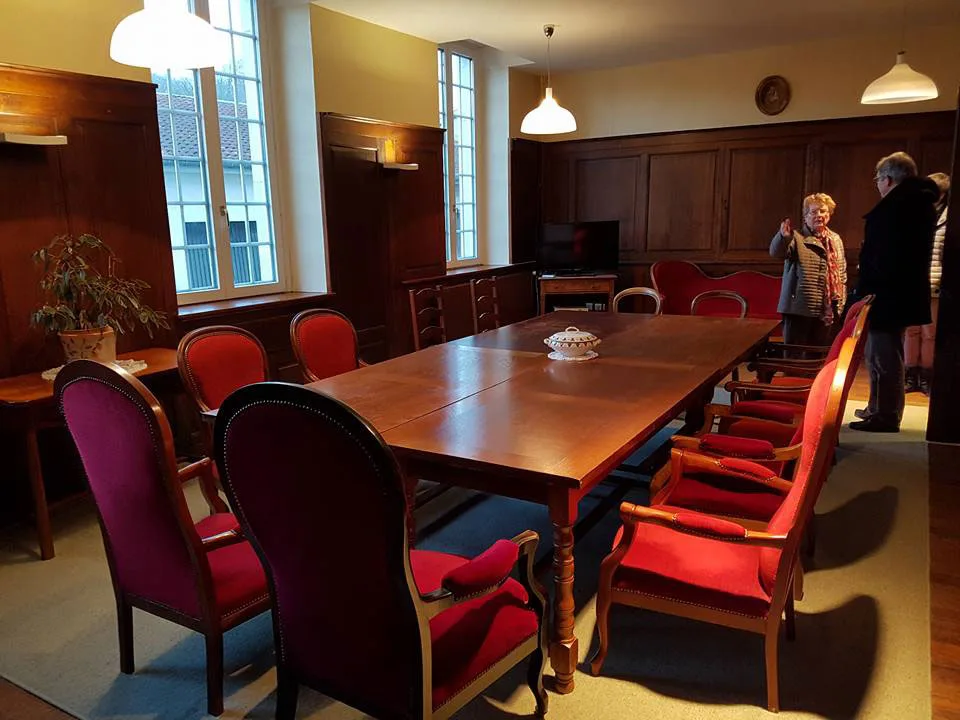 Salle de réunion bourgeoise avec grande table en bois et fauteuils rouges, boiseries et fenêtres