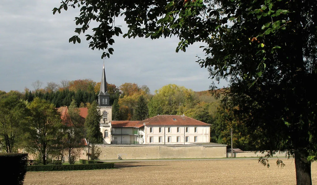 Vue depuis la campagne du hameau de Benoîte-Vaux avec clocher et bâtiment du centre d'accueil
