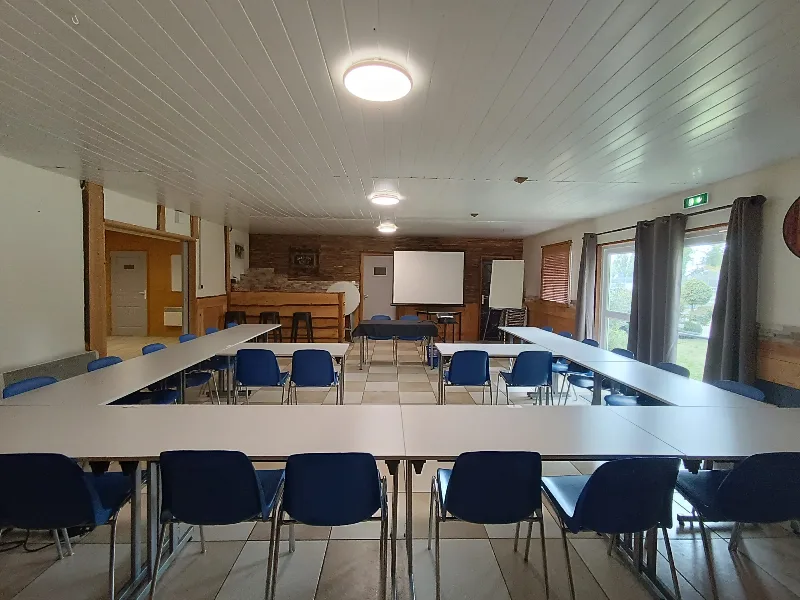 Salle de séminaire de 100 m² en configuration U avec tables blanches, chaises bleues et écran