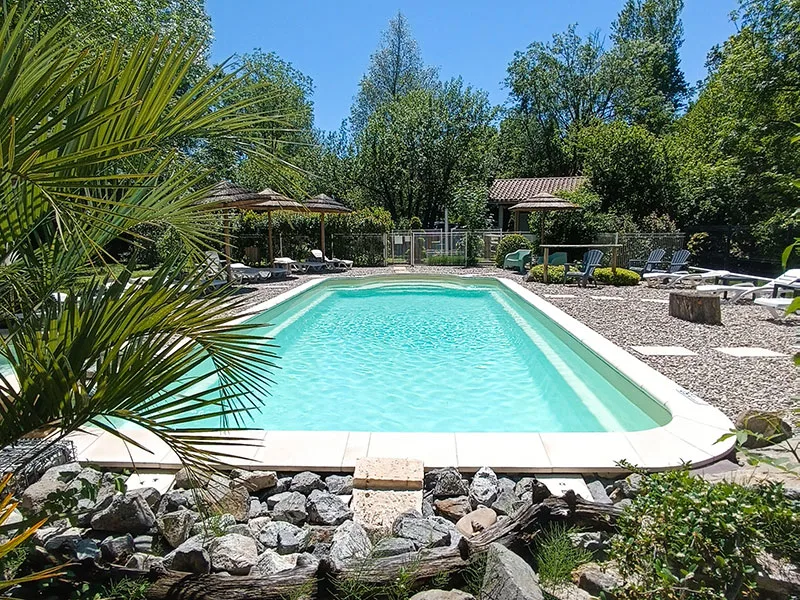 Piscine privée rectangulaire avec transats et parasols entourée de végétation méditerranéenne