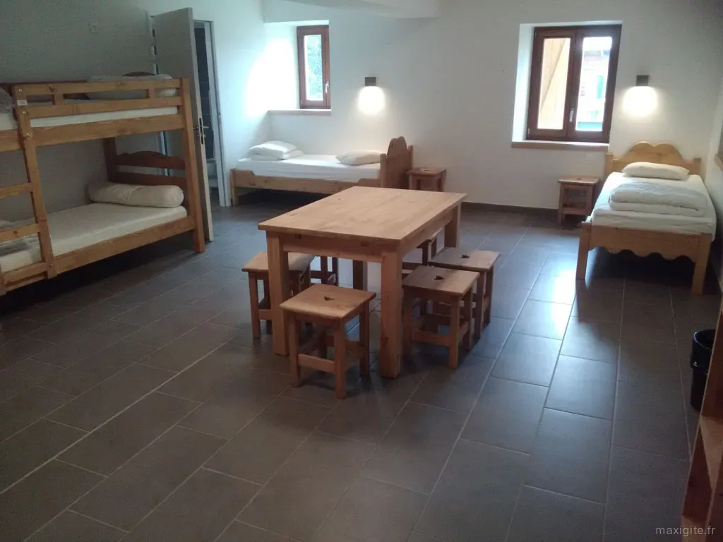 Dortoir collectif avec lits superposés, lits simples en bois et table en bois