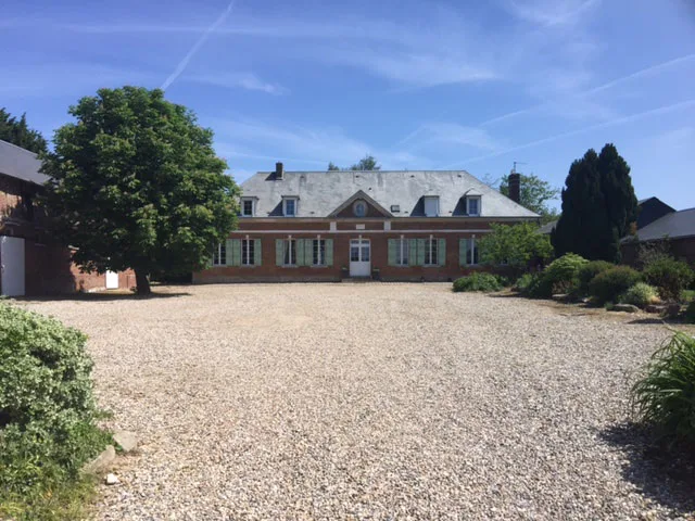 Façade principale du manoir en brique avec grande cour de gravier et ciel bleu