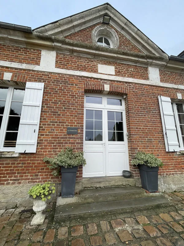 Entrée du bâtiment en brique avec porte blanche à volets et pots de plantes sur les marches