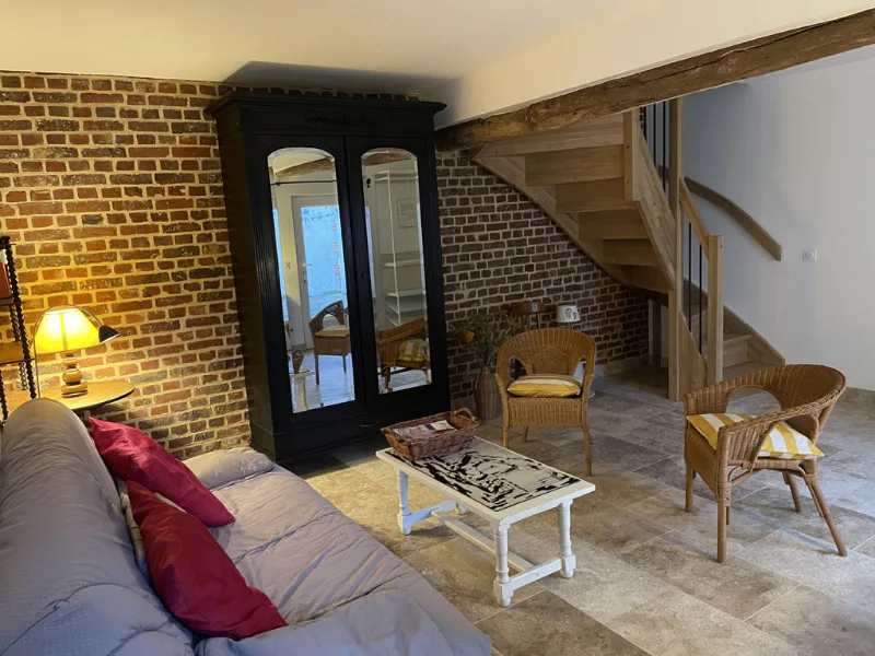 Salon intérieur avec murs en briques apparentes, canapé rouge, fauteuils et escalier bois