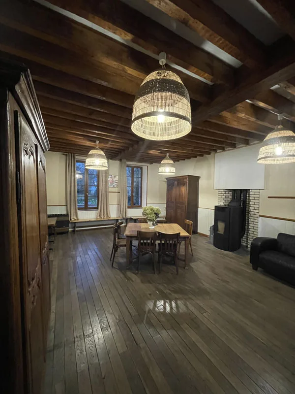 Grand salon avec poutres en bois sombres, lustre en cristal, plancher bois et cheminée