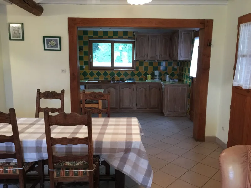Séjour avec coin repas, table à carreaux et chaises en bois, cuisine ouverte en fond