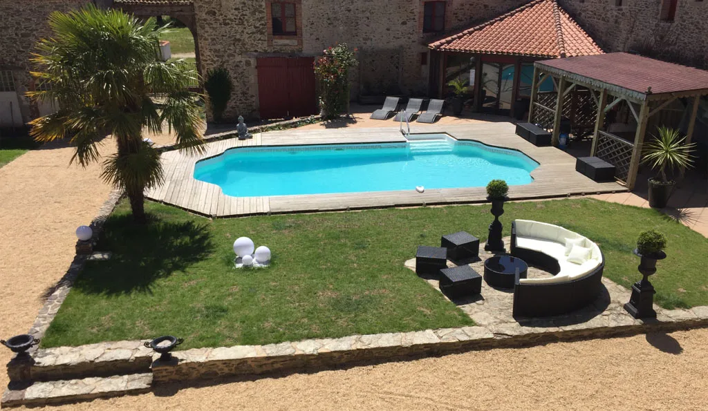 Vue aérienne piscine avec terrasse bois, palmier et salon de jardin