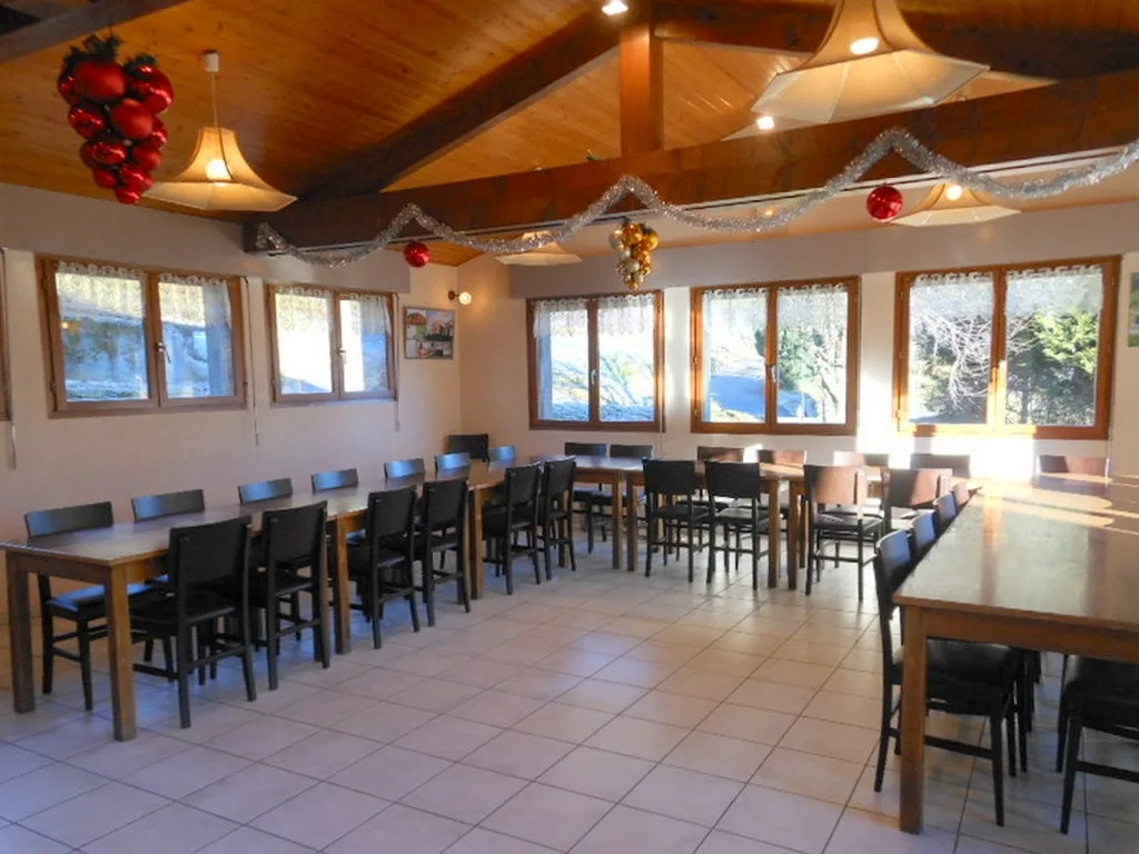 Grande salle a manger avec plafond en bois, tables et chaises noires pour trente convives, decorations de Noel