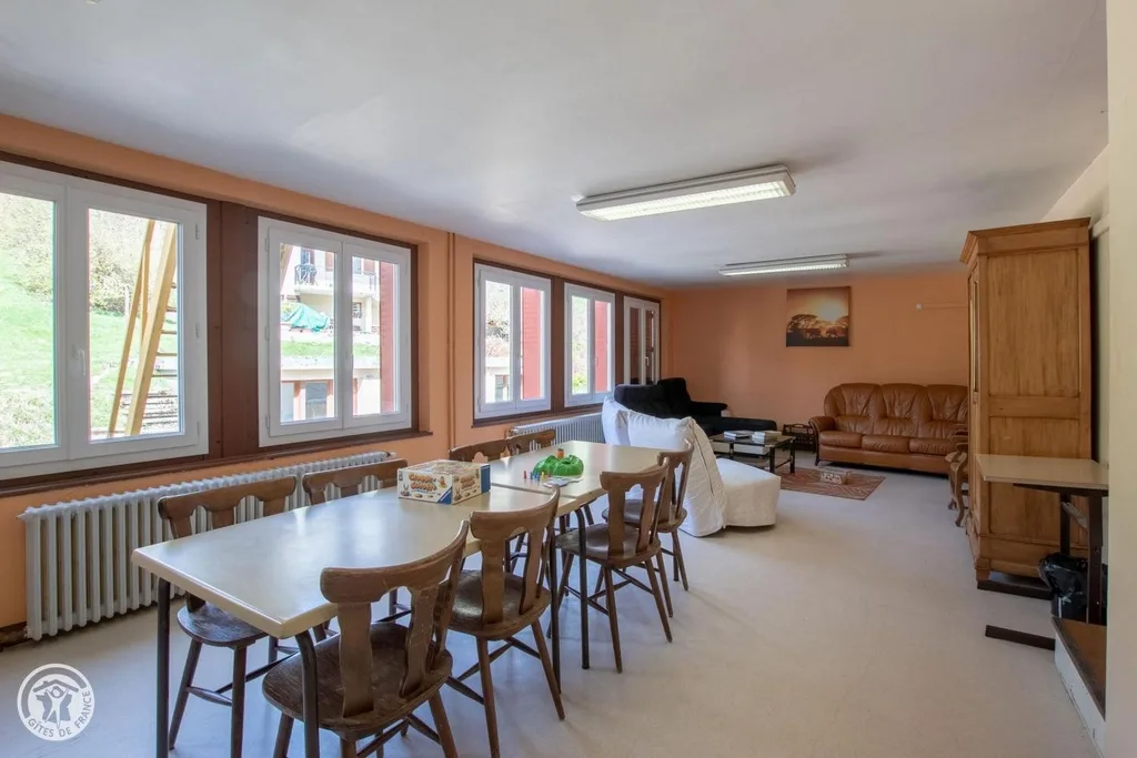 Salon commun avec table et chaises en bois, jeux de societe, canapes en cuir brun, grandes fenetres et murs saumon