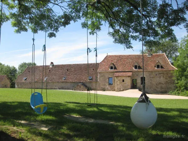 Aire de jeux avec balançoires sous les grands arbres devant les bâtiments en pierre