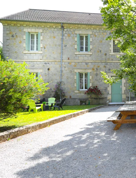 Façade arrière en pierre avec volets verts, mobilier de jardin et table de pique-nique