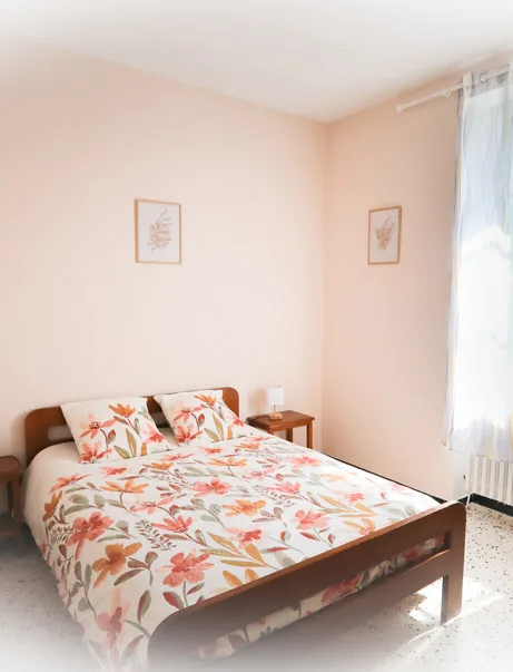 Chambre double avec lit fleuri, murs roses et cadres décoratifs
