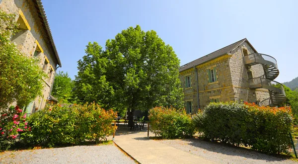 Façade en pierre du Colombier avec grand arbre et jardin fleuri sous le ciel bleu