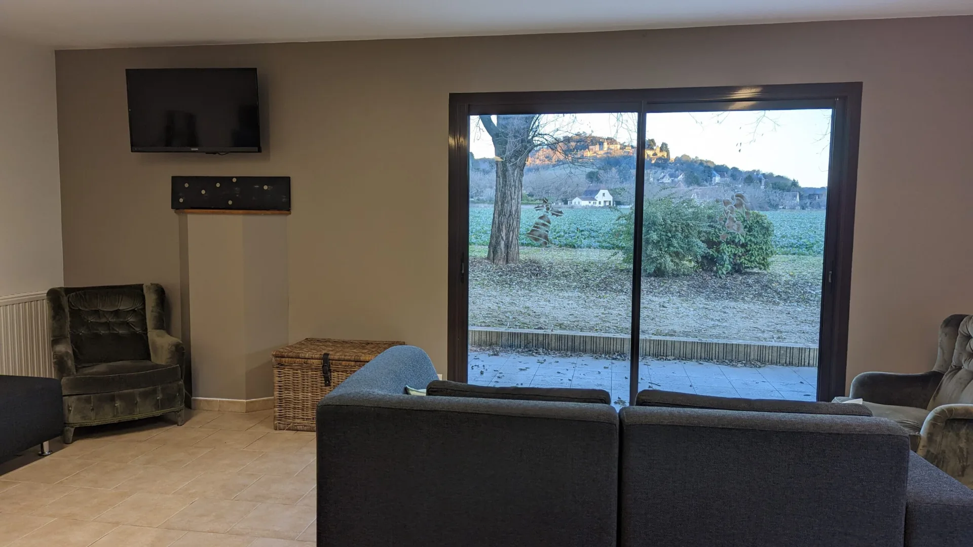 Coin salon avec canapes, fauteuil, television et grande baie vitree ouvrant sur le jardin