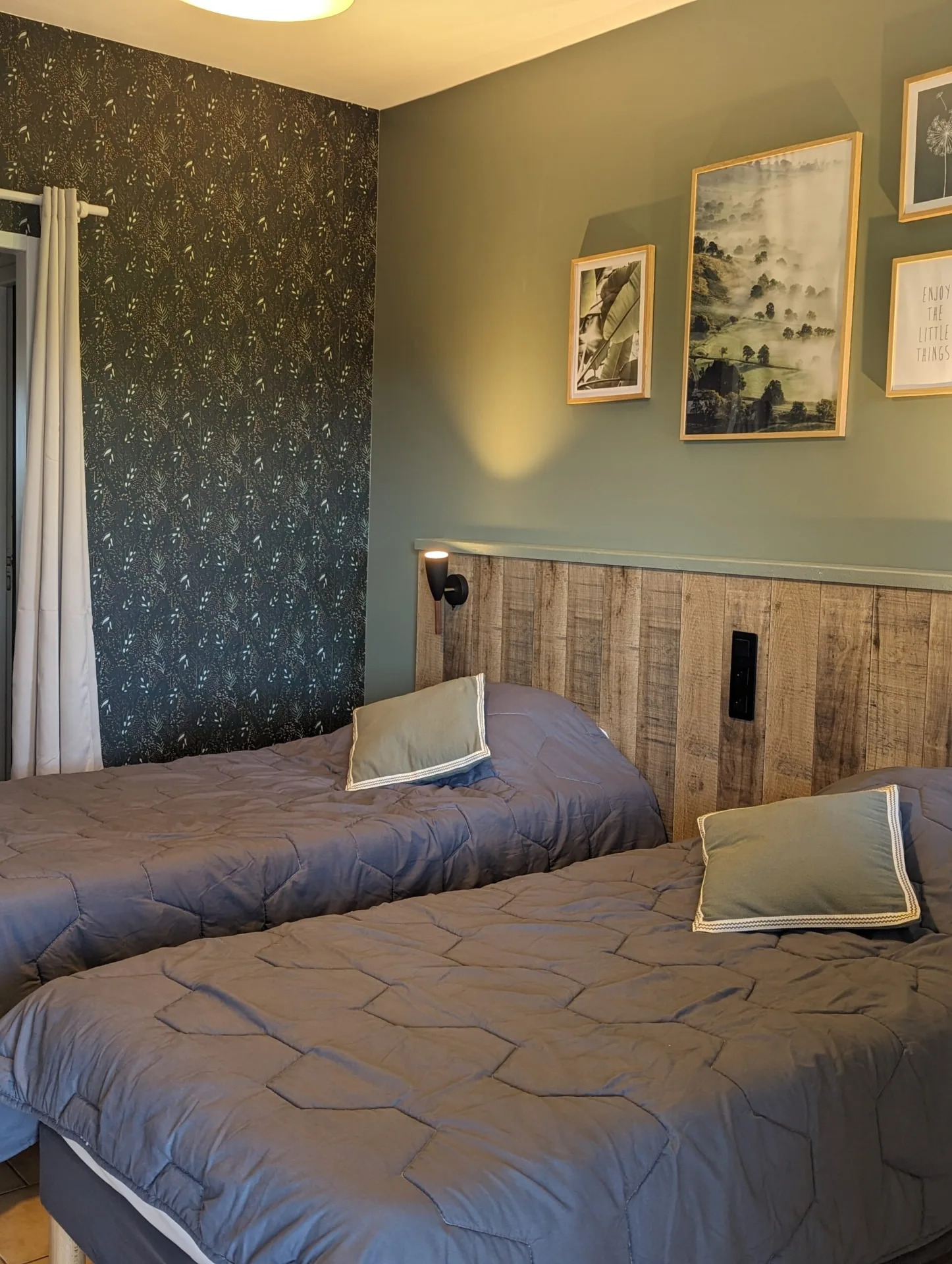 Chambre double aux murs vert sauge avec tete de lit en bois, coussins et cadres decoratifs