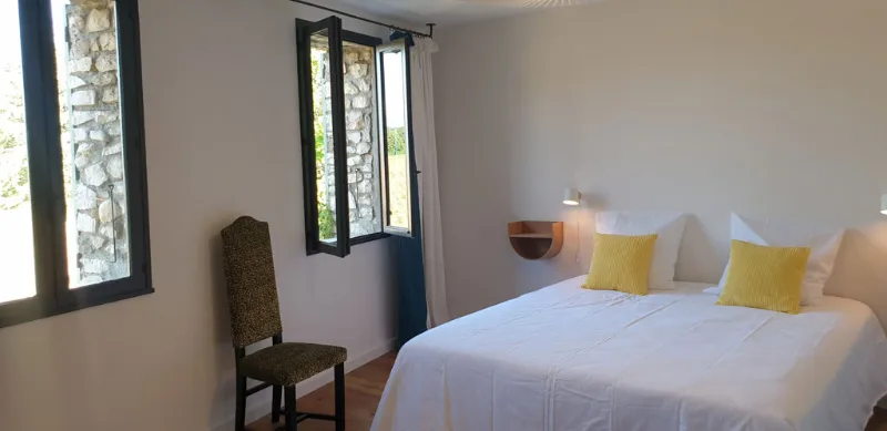 Chambre claire avec lit double, coussins jaunes et fenêtres à encadrement en pierre apparente