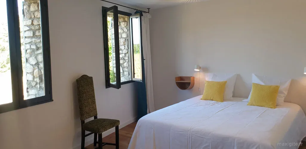 Chambre claire avec lit double, coussins jaunes et fenêtres à encadrement en pierre apparente