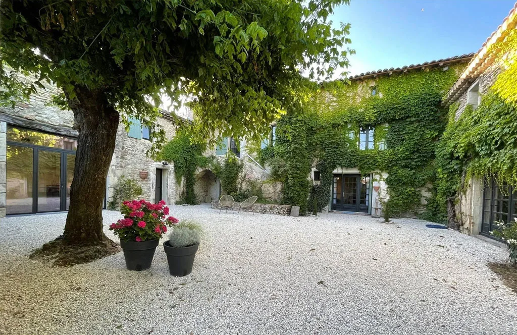 Gîte de groupe La Cour Joyeuse à La Bâtie-Rolland — Cour intérieure en gravier avec bâtiments en pierre couverts de lierre et grand arbre centenaire, capacité 16 personnes