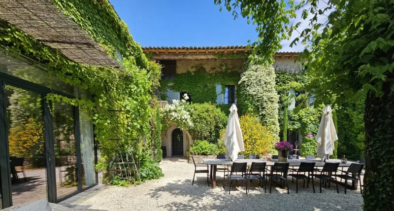 Terrasse ombragée avec grande table dressée sous des parasols blancs et façade verdoyante fleurie