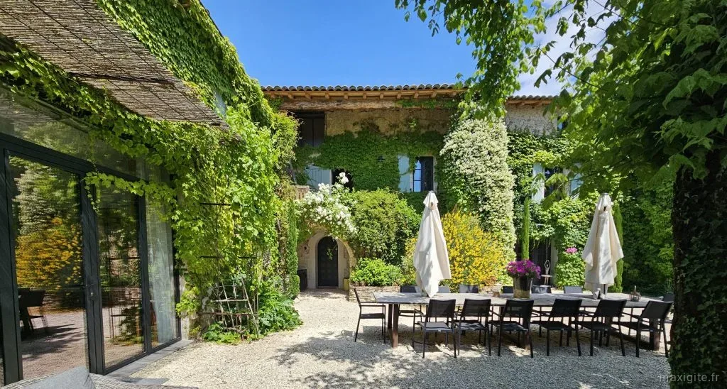 Terrasse ombragée avec grande table dressée sous des parasols blancs et façade verdoyante fleurie
