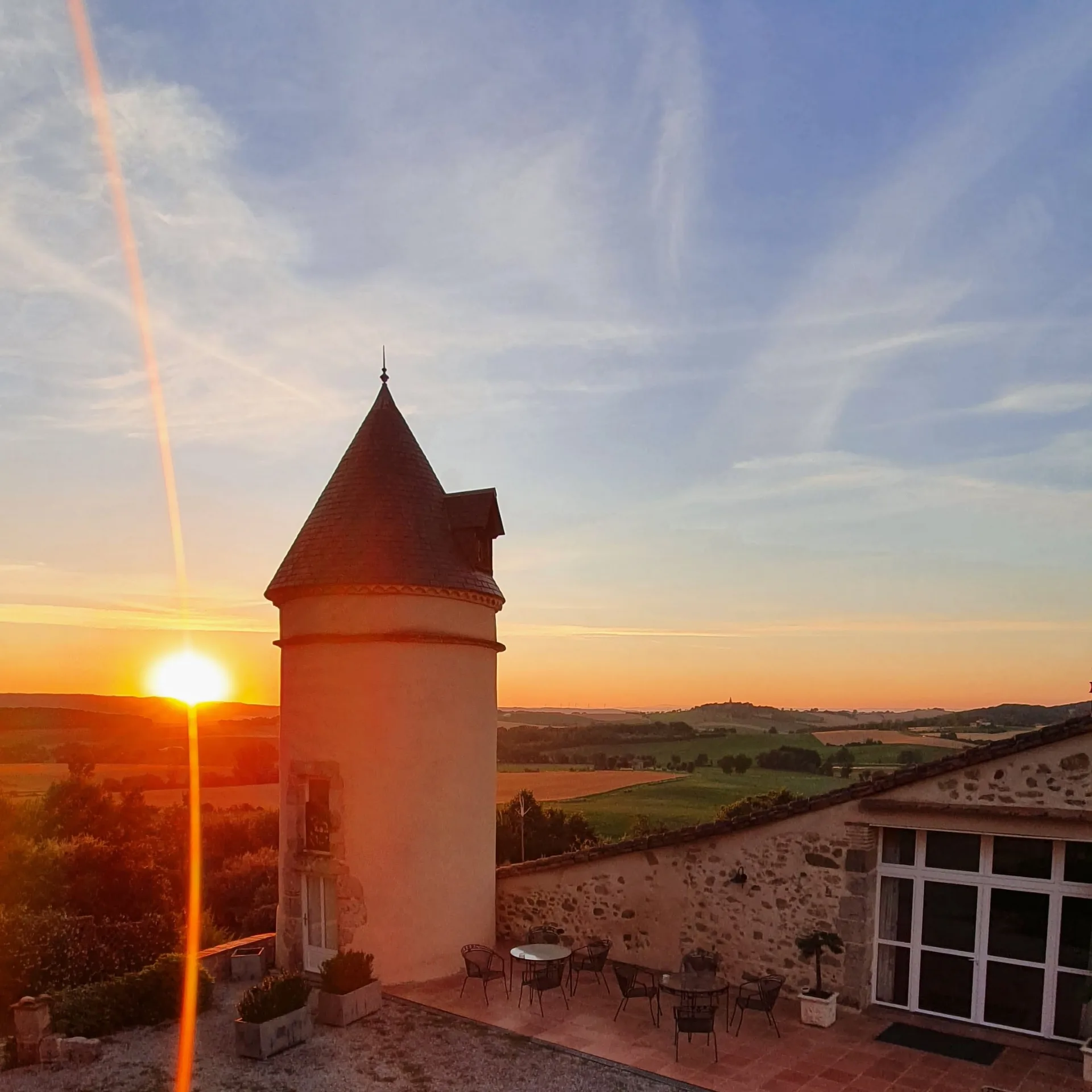 Façade en pierre et briques avec fenêtres cintrées, lavande au premier plan et panorama sur les collines du Tarn