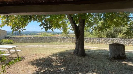 Vue panoramique sur la campagne depuis la terrasse couverte avec arbre et muret en pierre au premier plan