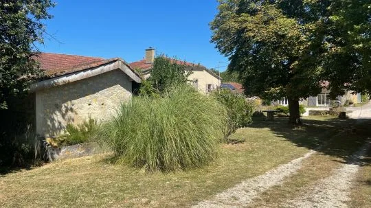 Parc du hameau avec bâtiments en pierre, graminées ornementales et pelouse ombragée sous de grands arbres