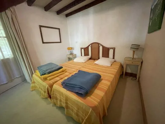 Chambre avec deux lits jumeaux à couvre-lits rayés jaunes, poutres apparentes au plafond et tables de chevet