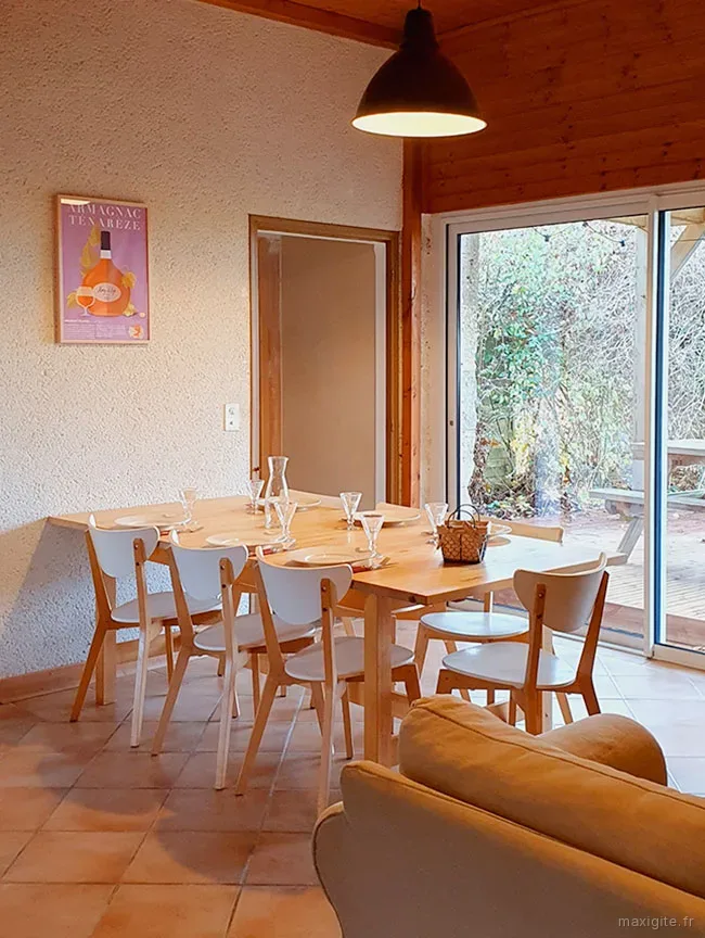 Salle à manger du gîte Ténarèze avec table dressée pour huit convives, plafond en bois, baie vitrée et affiche Armagnac