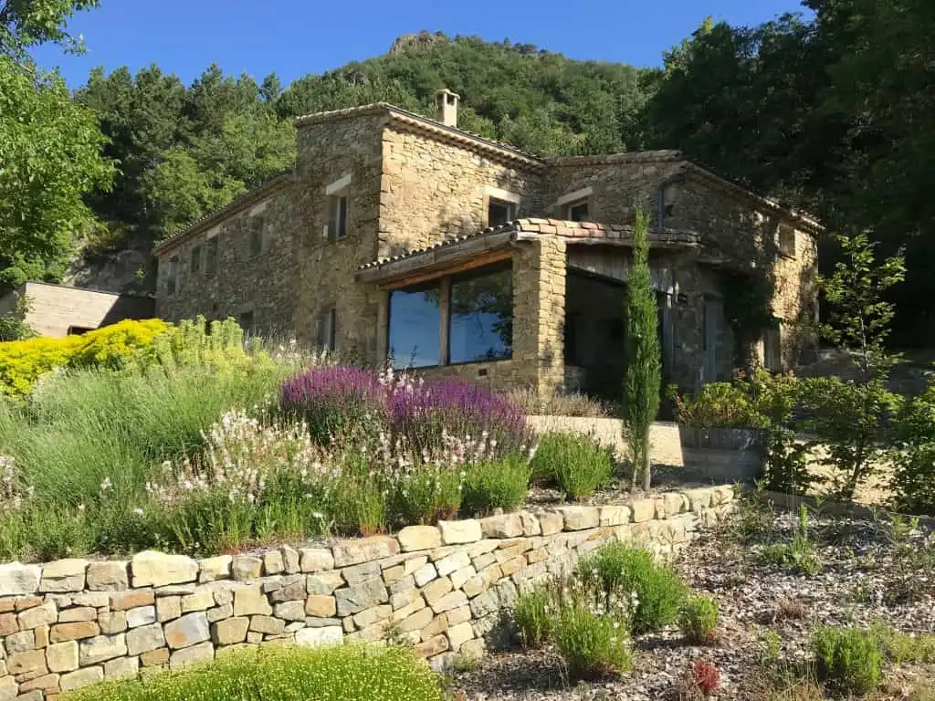 Espace de vie extérieur couvert en pierre avec terrasse ombragée, mobilier en bois et vue sur le jardin paysager