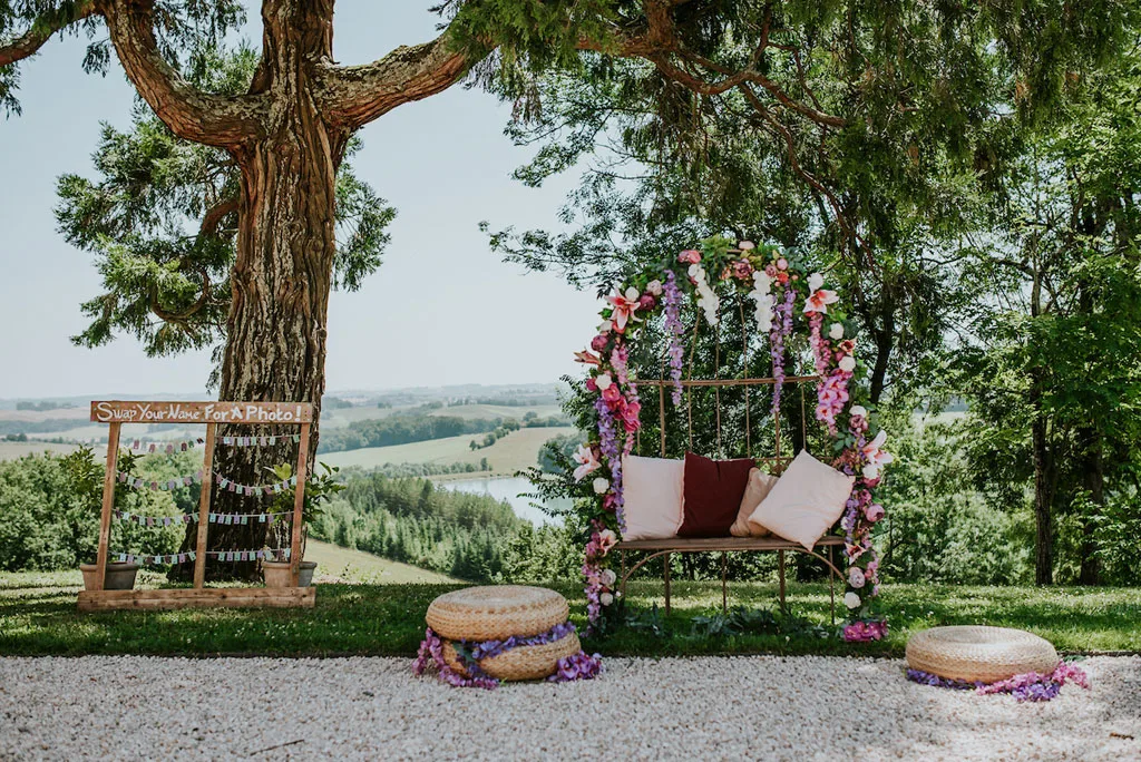 Arche florale de cérémonie sous un grand arbre avec vue panoramique sur la campagne gersoise