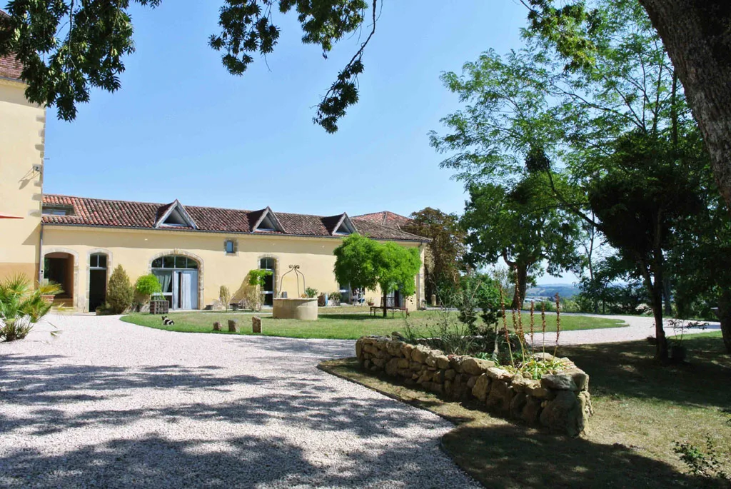 Vue extérieure des bâtiments du domaine avec fontaine en pierre et jardin arboré verdoyant