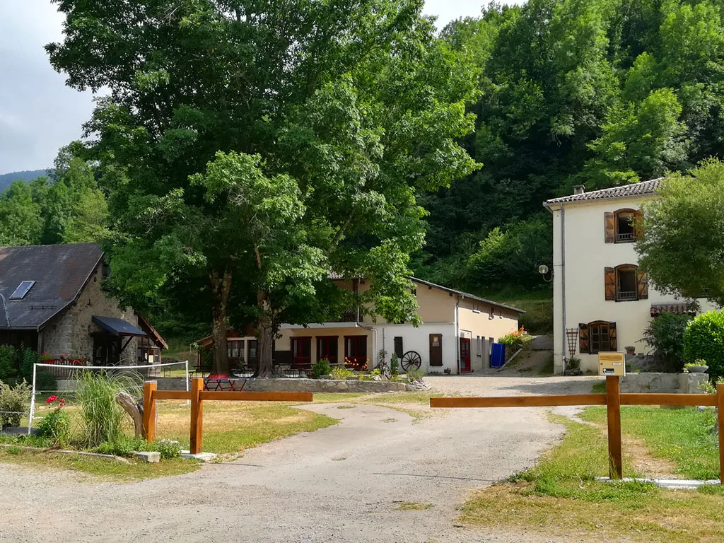 Cour centrale du domaine avec bâtiment blanc à étages, grange en pierre restaurée, arbres et clôture en bois au premier plan