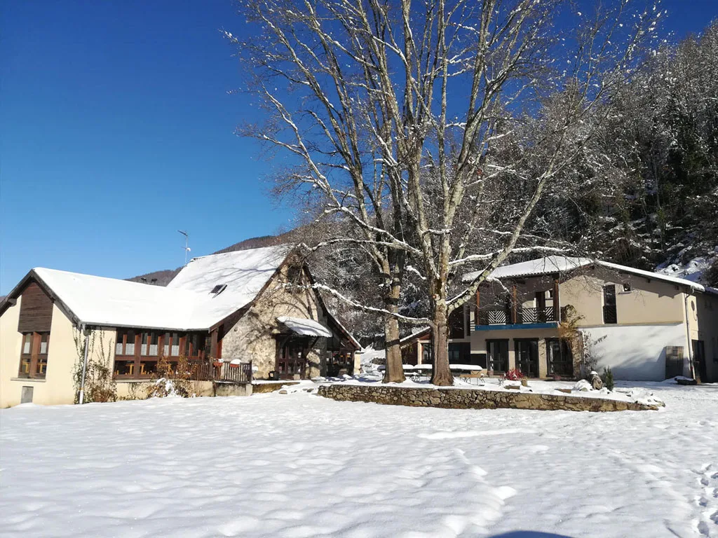 Le domaine L'Escalusse sous la neige en hiver avec bâtiments aux toits blancs, grand arbre dépouillé et ciel bleu