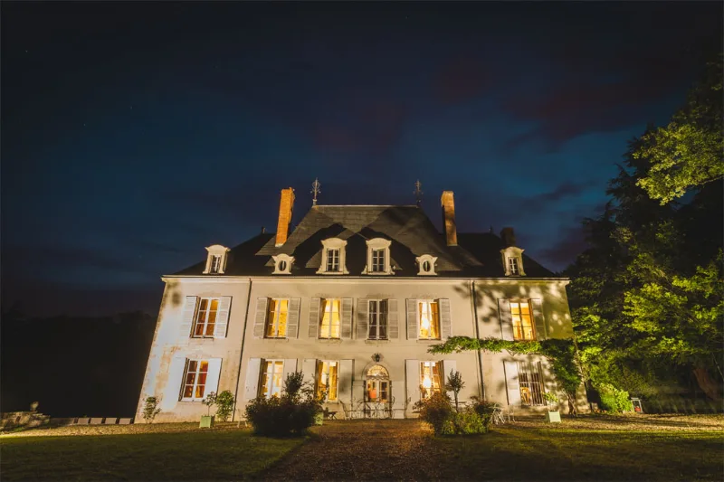 Façade du Château de Beaumont illuminée de nuit avec pelouse verte au premier plan et arbres