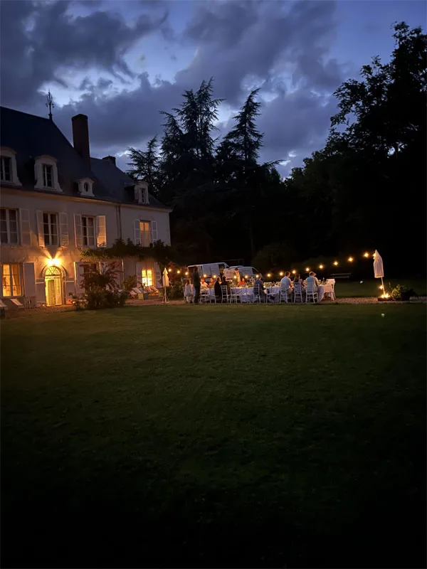 Vue nocturne du château depuis le parc avec éclairage chaleureux sur la façade en pierre blanche