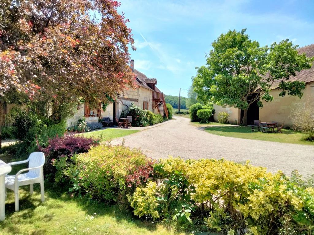 Gîte de groupe La Ferme des Pignons à Saint-Martin-des-Bois — Facade principale de la ferme en pierre avec toit en tuiles entouree d'arbres et de haies fleuries, capacité 26 personnes