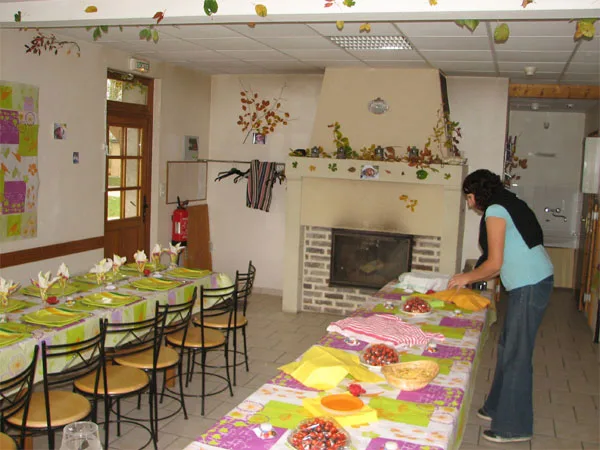 Grande salle commune dressee pour un repas de groupe avec tables et nappes colorees