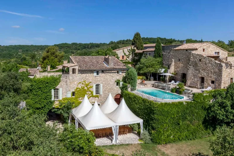 Vue aérienne du domaine avec bâtiments en pierre, piscine et tentes blanches au milieu des arbres