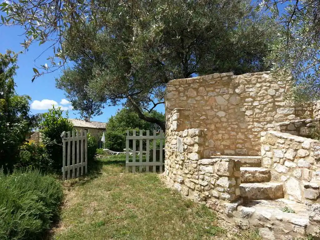 Terrasse en pierre avec salon de jardin bleu ombragé par la végétation méditerranéenne