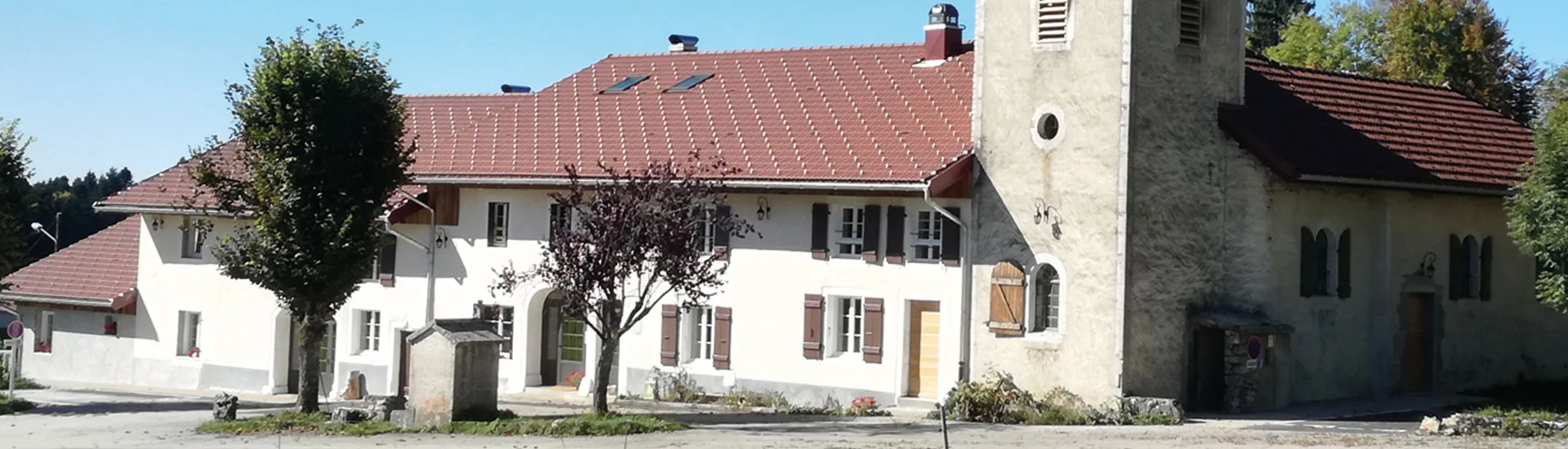 Gîte de groupe L'Ermitage des Frasses à Grande-Rivière Château — Façade blanche du gîte avec toit en tuiles rouges, balcon en bois et jardin verdoyant au pied du Haut-Jura, capacité 56 personnes