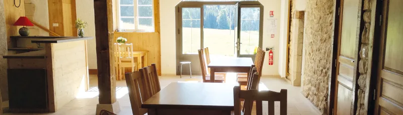 Grande salle à manger lumineuse avec tables et chaises en bois massif face aux fenêtres donnant sur le paysage
