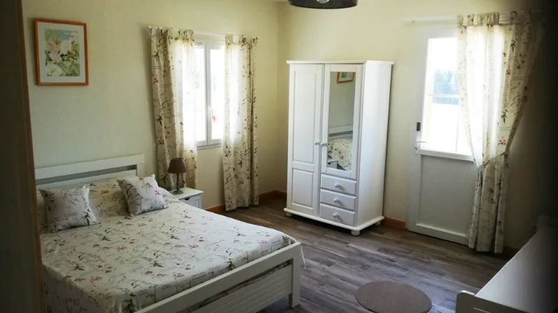 Chambre lumineuse avec mobilier blanc, rideaux clairs et fenêtres donnant sur la campagne jurassienne
