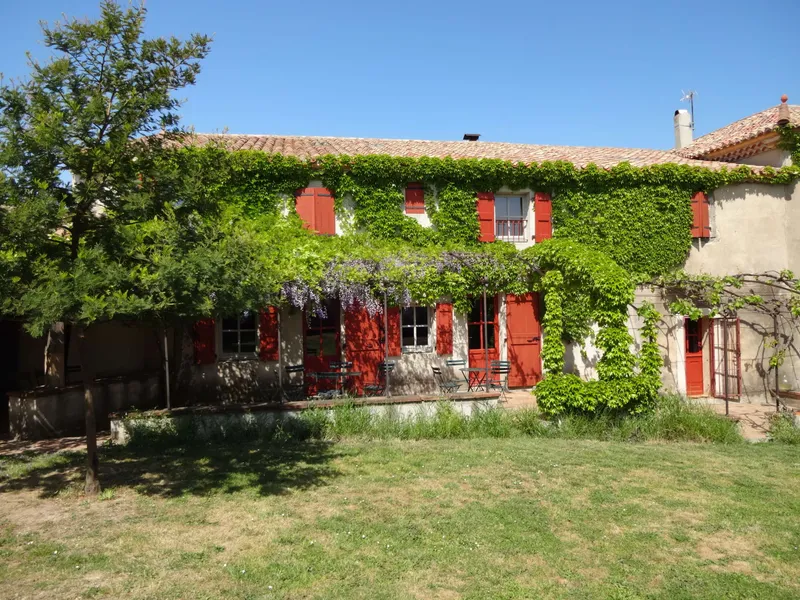 Façade en pierre couverte de vigne vierge et volets rouges du mas viticole sous un ciel bleu