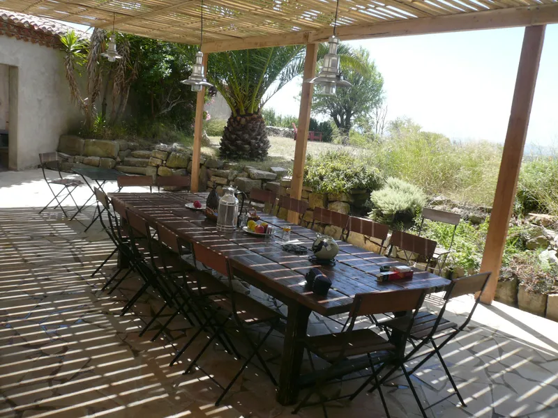Longue table dressée pour le petit-déjeuner sous une pergola en bambou face à la campagne